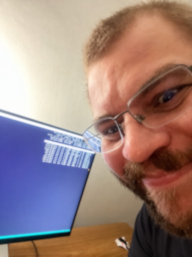 Fernando grinning at the camera next to a monitor full of terminal output